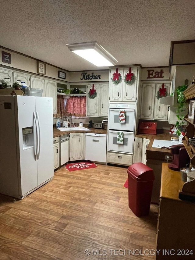 kitchen with a textured ceiling, white appliances, and light hardwood / wood-style flooring