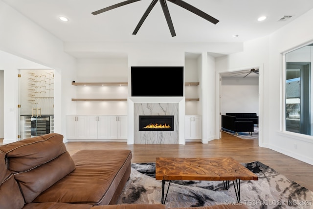 living room featuring built in shelves, ceiling fan, a high end fireplace, and hardwood / wood-style floors