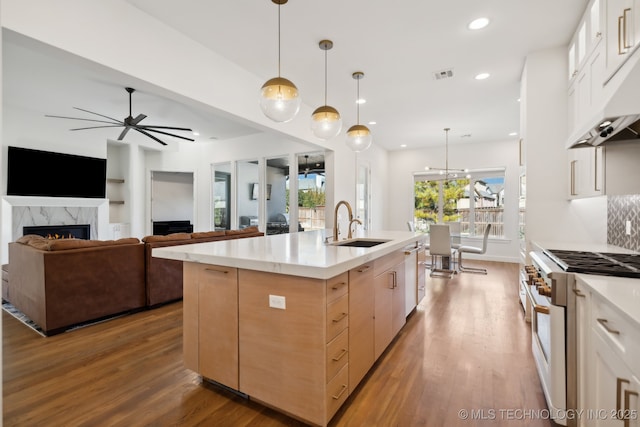 kitchen featuring sink, gas range oven, white cabinets, a center island with sink, and decorative light fixtures