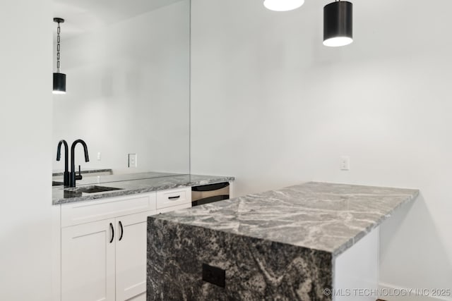 kitchen with sink, hanging light fixtures, white cabinets, and stone countertops