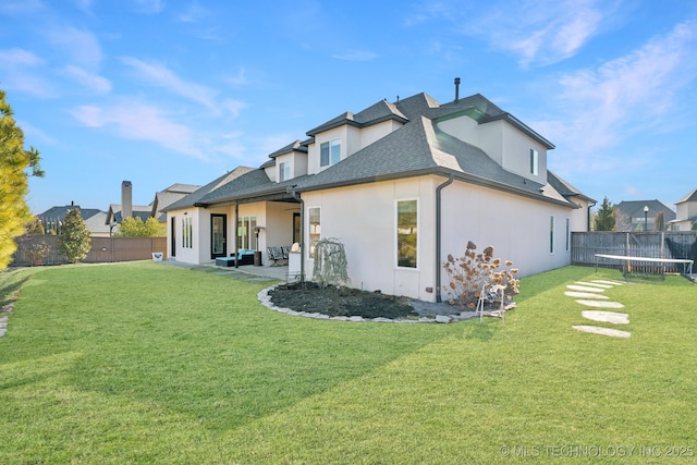 rear view of property with a lawn, a trampoline, and a patio area