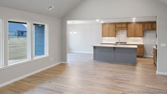 kitchen with vaulted ceiling, decorative light fixtures, a kitchen island with sink, and light hardwood / wood-style flooring