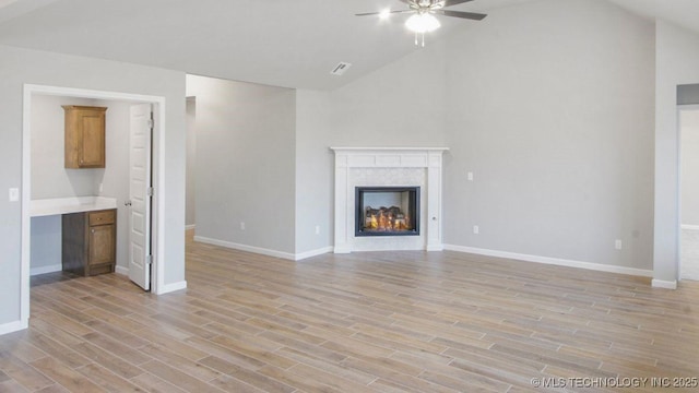 unfurnished living room featuring ceiling fan, a high end fireplace, high vaulted ceiling, and light hardwood / wood-style flooring