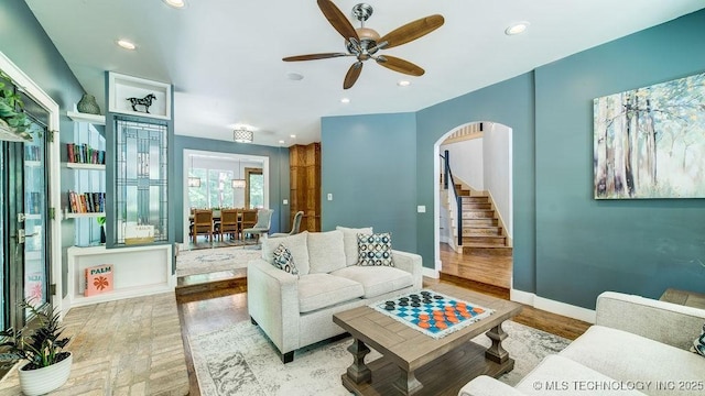 living area featuring ceiling fan, arched walkways, stairs, baseboards, and wood finished floors