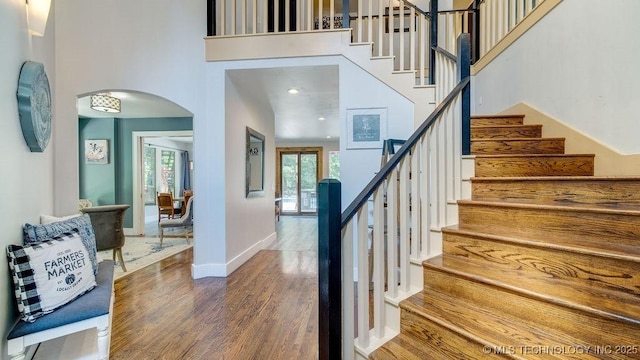 staircase with baseboards, arched walkways, a towering ceiling, and wood finished floors