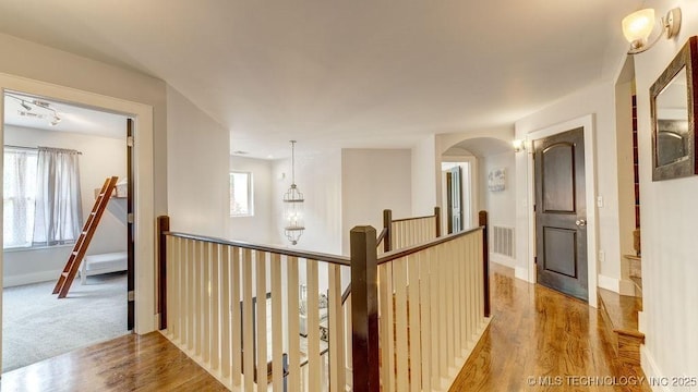 hall featuring baseboards, visible vents, wood finished floors, and an upstairs landing