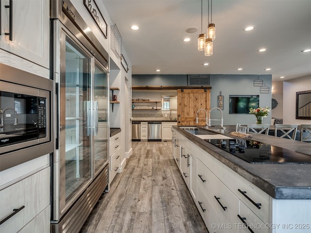 kitchen featuring a sink, built in appliances, light wood finished floors, and white cabinetry