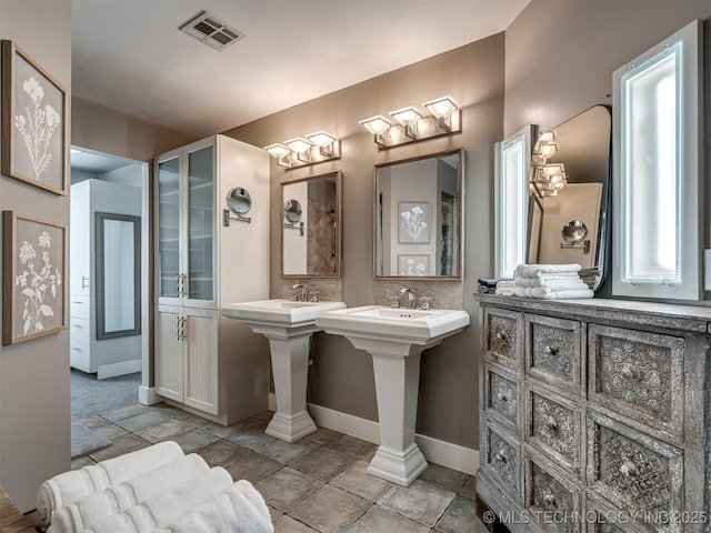 full bathroom with baseboards, two sinks, and visible vents