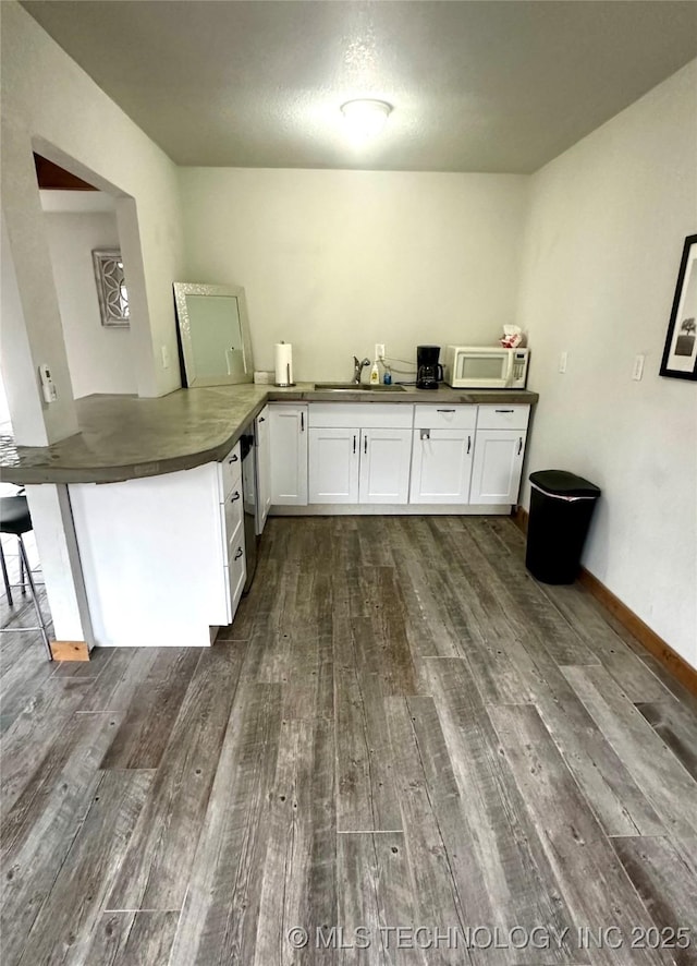 kitchen featuring dark countertops, white microwave, a sink, white cabinetry, and dark wood-type flooring