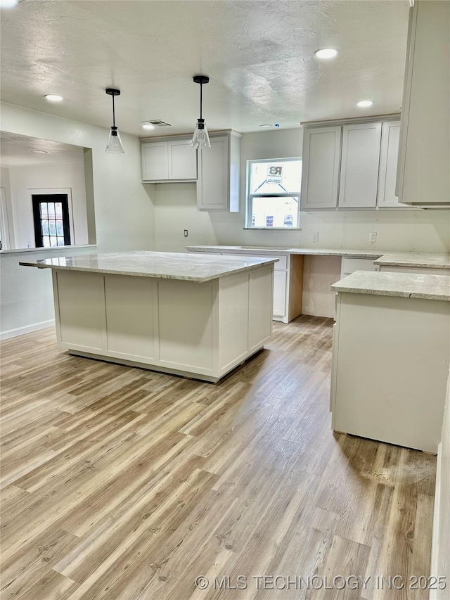 kitchen featuring light stone counters, a kitchen island, and hanging light fixtures