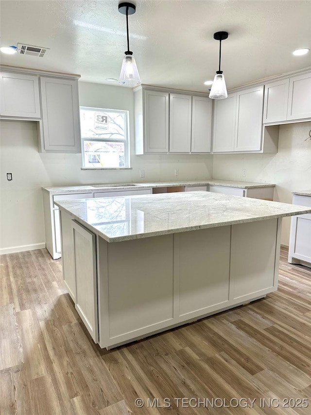 kitchen with light stone counters, a kitchen island, decorative light fixtures, light hardwood / wood-style flooring, and white cabinetry