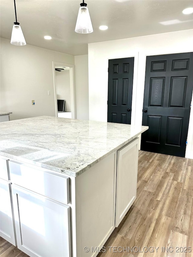 kitchen featuring white cabinets, decorative light fixtures, light stone counters, and light hardwood / wood-style floors