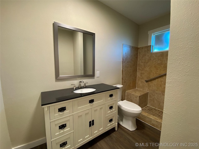 bathroom featuring tiled shower, hardwood / wood-style floors, vanity, and toilet