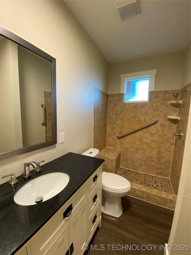 bathroom with vanity, toilet, wood-type flooring, and a tile shower