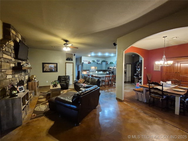 living room with ceiling fan with notable chandelier, concrete flooring, and a fireplace