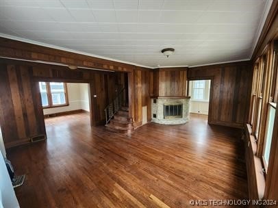 unfurnished living room featuring wood walls, dark hardwood / wood-style flooring, ornamental molding, and a fireplace