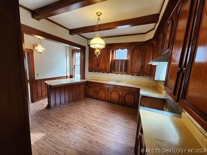 kitchen with beam ceiling, kitchen peninsula, light hardwood / wood-style flooring, and hanging light fixtures