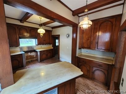 kitchen featuring beam ceiling, dark brown cabinets, decorative light fixtures, and light wood-type flooring