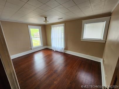 empty room with dark hardwood / wood-style floors and crown molding