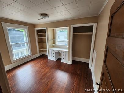 unfurnished bedroom with multiple windows, two closets, and dark hardwood / wood-style floors