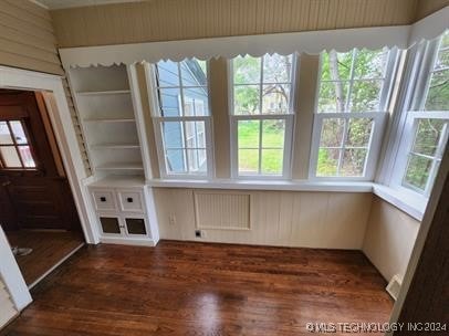 interior space with dark hardwood / wood-style flooring, radiator, and wood walls