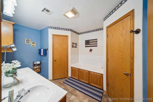 bathroom with visible vents, a garden tub, double vanity, wood finished floors, and a sink