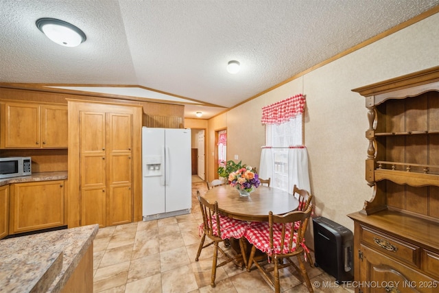 kitchen featuring stainless steel microwave, lofted ceiling, white refrigerator with ice dispenser, and brown cabinetry