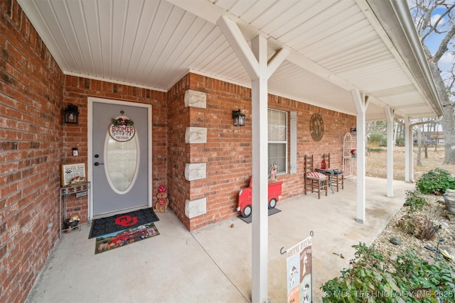 view of exterior entry with brick siding and a porch