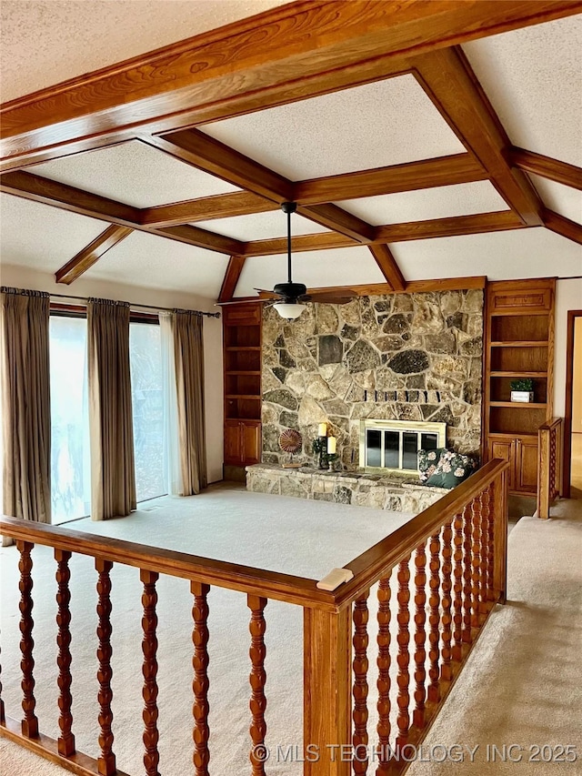 unfurnished living room featuring carpet flooring, built in shelves, ceiling fan, vaulted ceiling with beams, and a stone fireplace