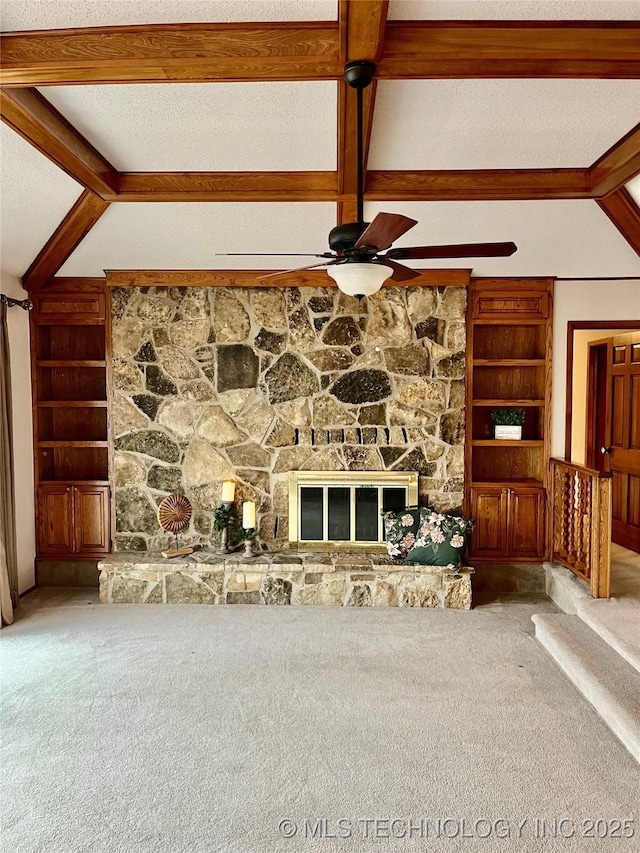 unfurnished living room featuring a stone fireplace, a ceiling fan, vaulted ceiling with beams, carpet floors, and built in features