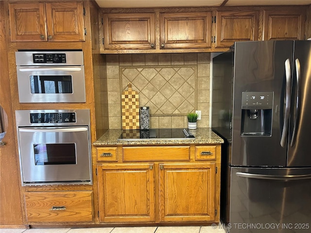 kitchen featuring brown cabinets, backsplash, fridge with ice dispenser, stone countertops, and black electric stovetop