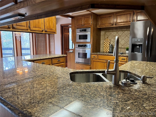 kitchen featuring brown cabinets, stainless steel fridge, tasteful backsplash, and dark stone countertops