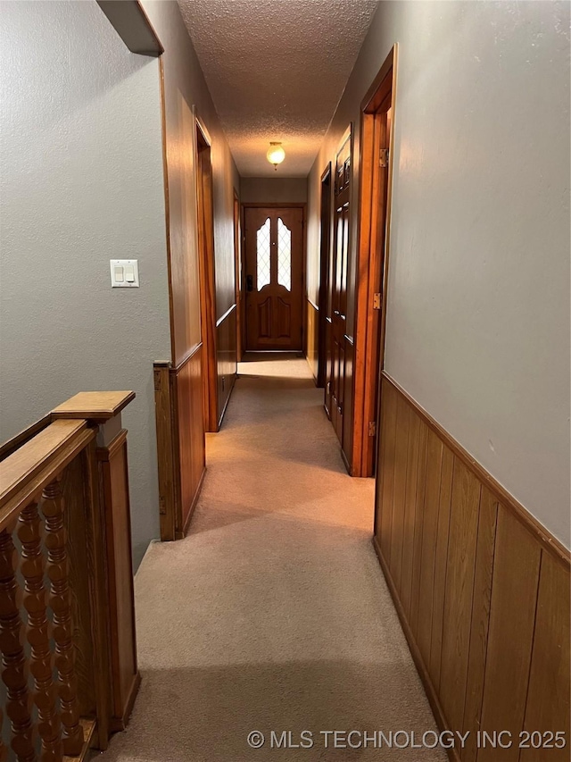 corridor featuring wooden walls, light carpet, and a textured ceiling