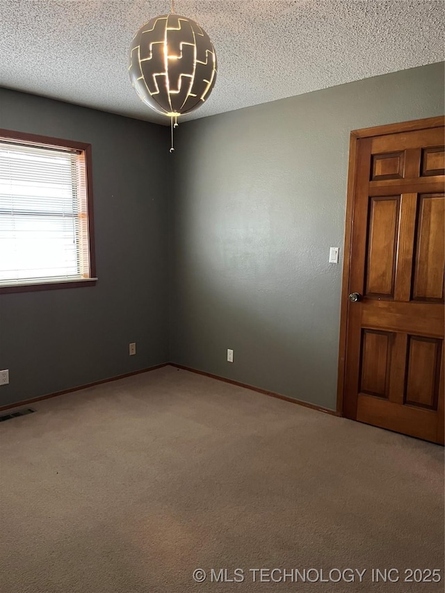 carpeted spare room featuring a textured ceiling and visible vents