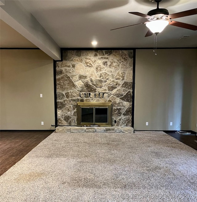 unfurnished living room featuring beam ceiling, a stone fireplace, ceiling fan, and carpet