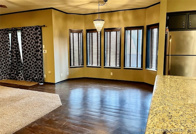 unfurnished dining area featuring ornamental molding, dark wood-type flooring, and an inviting chandelier