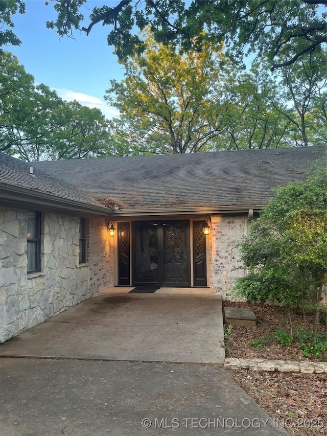entrance to property featuring stone siding and a shingled roof