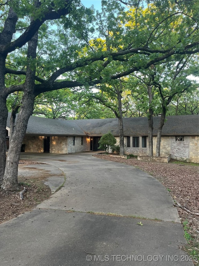 ranch-style home featuring driveway and stone siding