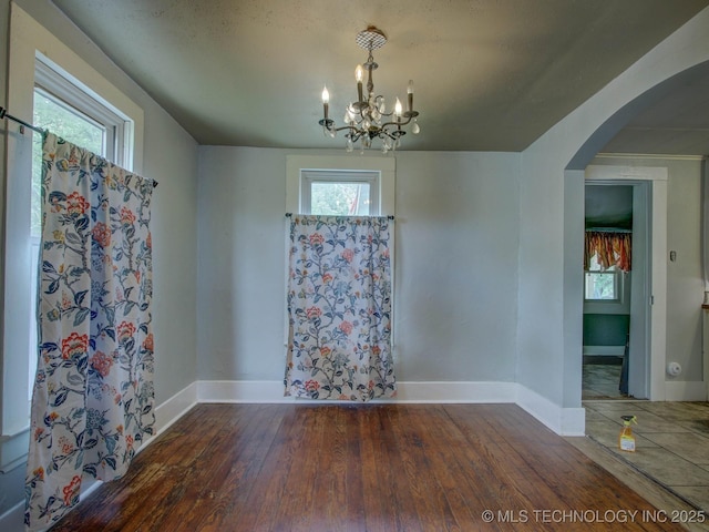 unfurnished dining area with a notable chandelier, dark hardwood / wood-style flooring, and plenty of natural light