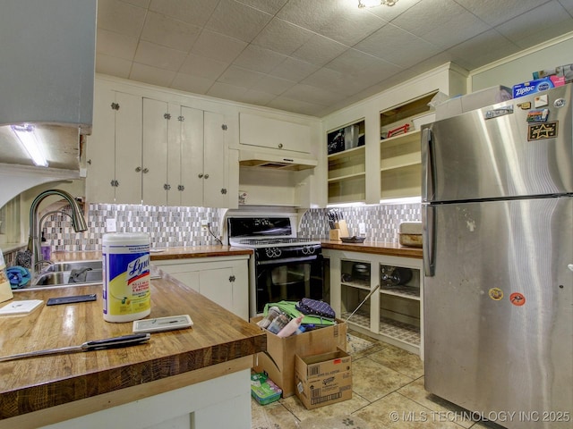 kitchen featuring backsplash, black stove, butcher block countertops, white cabinetry, and stainless steel refrigerator