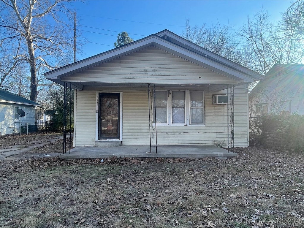 bungalow-style home featuring a porch and an AC wall unit