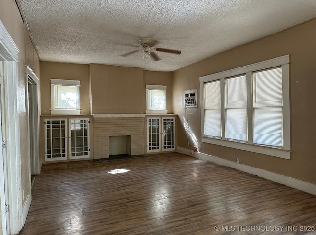 unfurnished living room featuring a wall mounted air conditioner, a brick fireplace, a textured ceiling, ceiling fan, and dark wood-type flooring