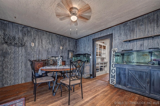 dining room with wood walls, ceiling fan, wood-type flooring, and ornamental molding