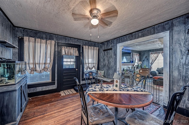 dining space with a textured ceiling, hardwood / wood-style flooring, ceiling fan, and wood walls