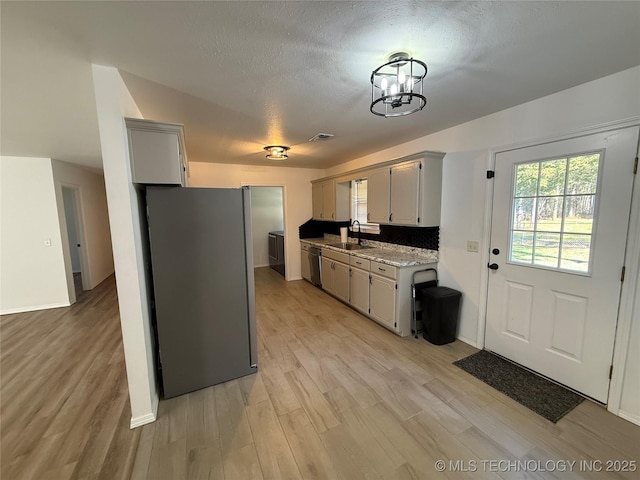 kitchen featuring sink, light hardwood / wood-style flooring, appliances with stainless steel finishes, tasteful backsplash, and a notable chandelier