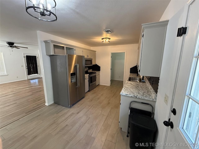 kitchen with light wood-type flooring, light stone counters, ceiling fan with notable chandelier, a textured ceiling, and stainless steel appliances