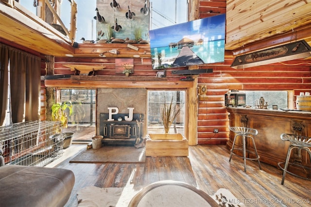 living room with rustic walls, a wood stove, a high ceiling, and hardwood / wood-style flooring