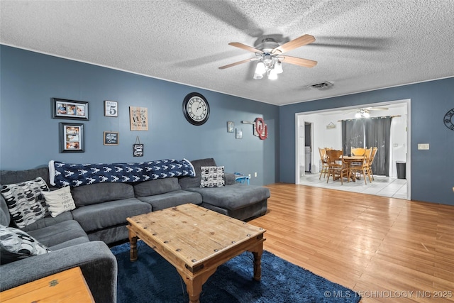 living room featuring ceiling fan, a textured ceiling, and light wood-type flooring