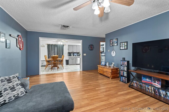 living room featuring ceiling fan, light hardwood / wood-style floors, and a textured ceiling