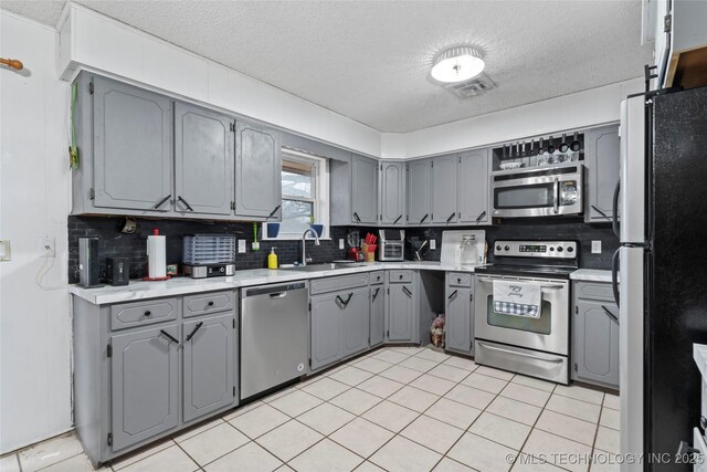 kitchen featuring gray cabinetry, backsplash, sink, a textured ceiling, and appliances with stainless steel finishes